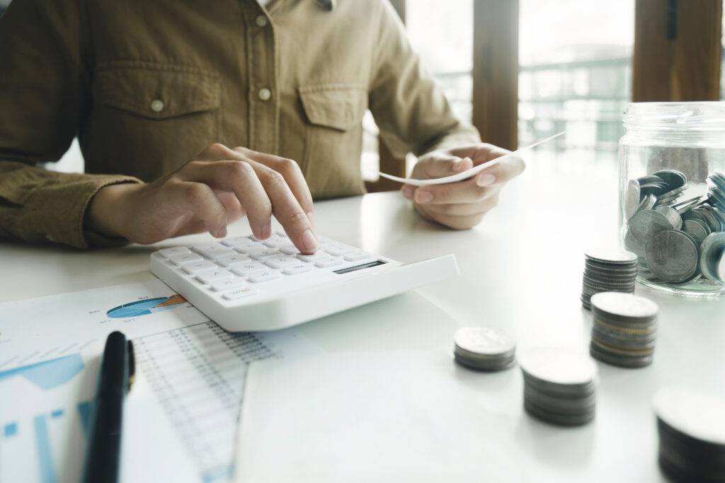 Woman accountant using a calculator and laptop computer while counting and discussing taxes with a client. Business audit and finance concepts